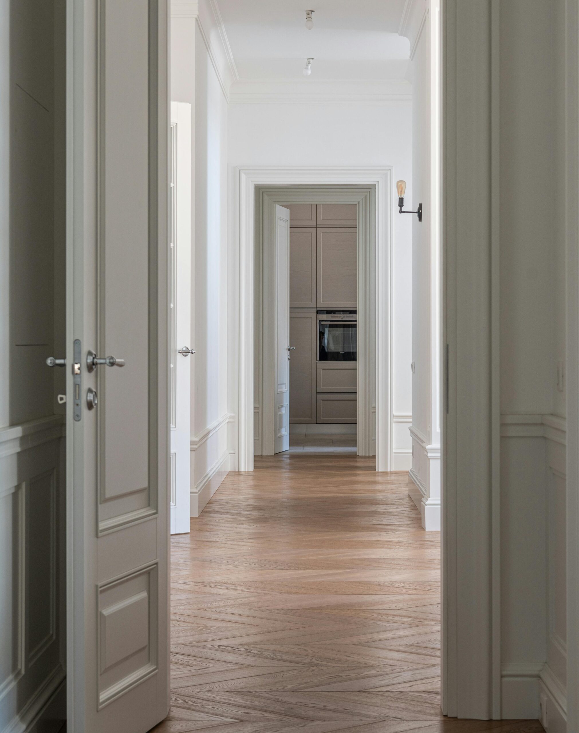 Bright hallway with wooden flooring and white walls leading to a room with built-in cabinets.