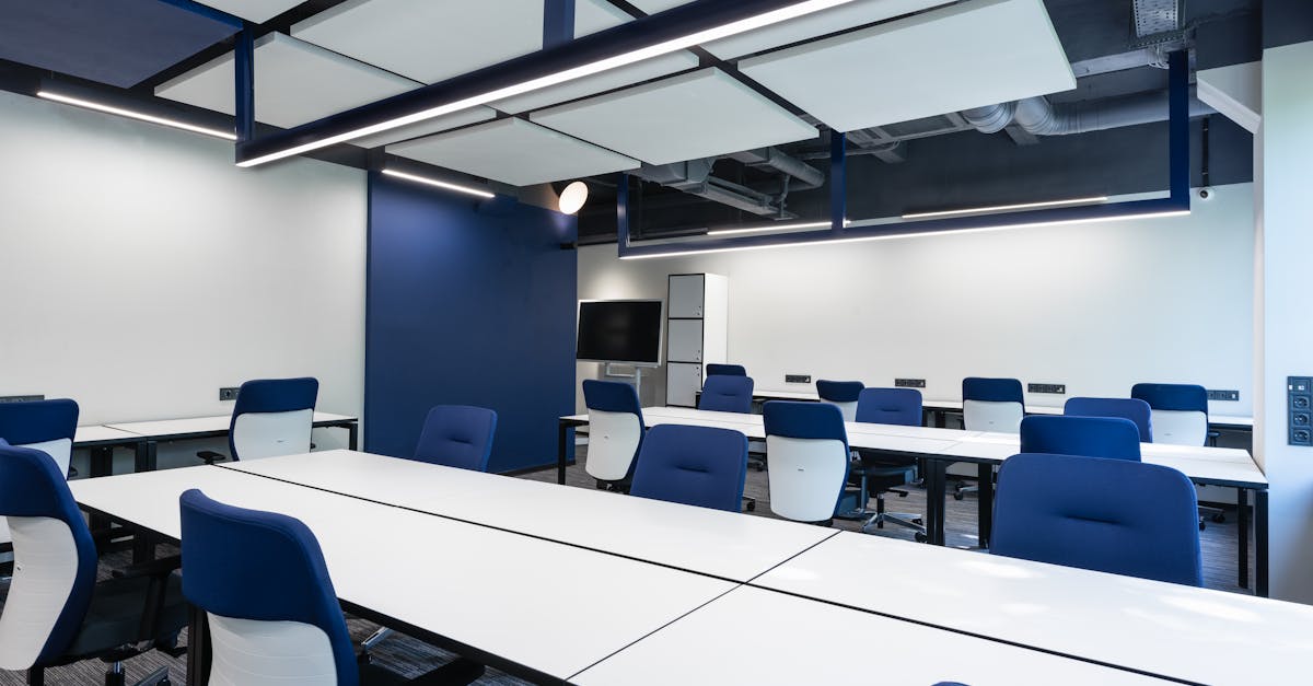 Interior of modern spacious workspace with long white tables and blue armchairs placed near monitor with black screen in business center